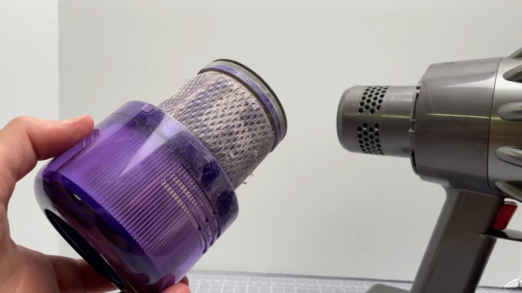 Ruka drži filter usisivača pre čišćenja, pored kućišta uređaja