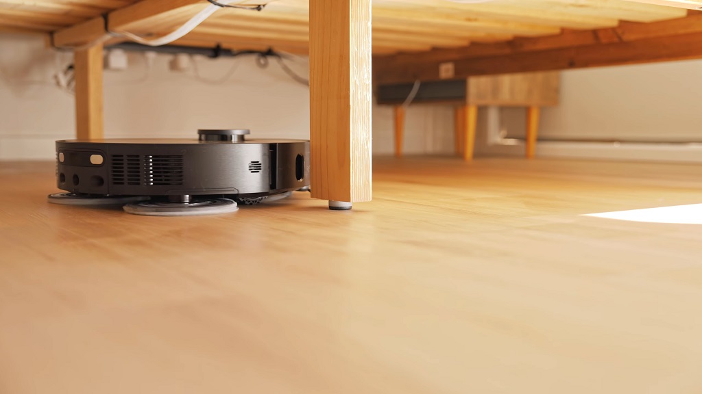 Robot usisivač čisti ispod kreveta na drvenom podu, dosežući teško dostupna mesta