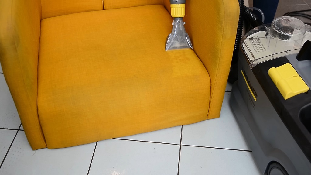 Dubinski usisivač uklanja mrlje sa žute fotelje tokom procesa prskanja i usisavanja