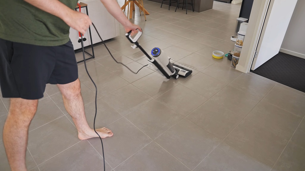 Osoba koristi štapni usisivač za čišćenje pločica u kuhinji.